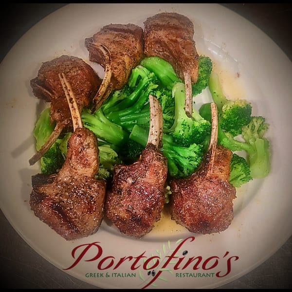 Six grilled lamb chops with bones, seasoned and served with bright green broccoli florets on a white plate.