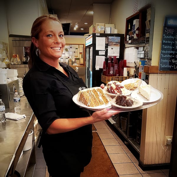 A smiling Portofino's waitress holds a tray with four slices of cake, ready to serve.