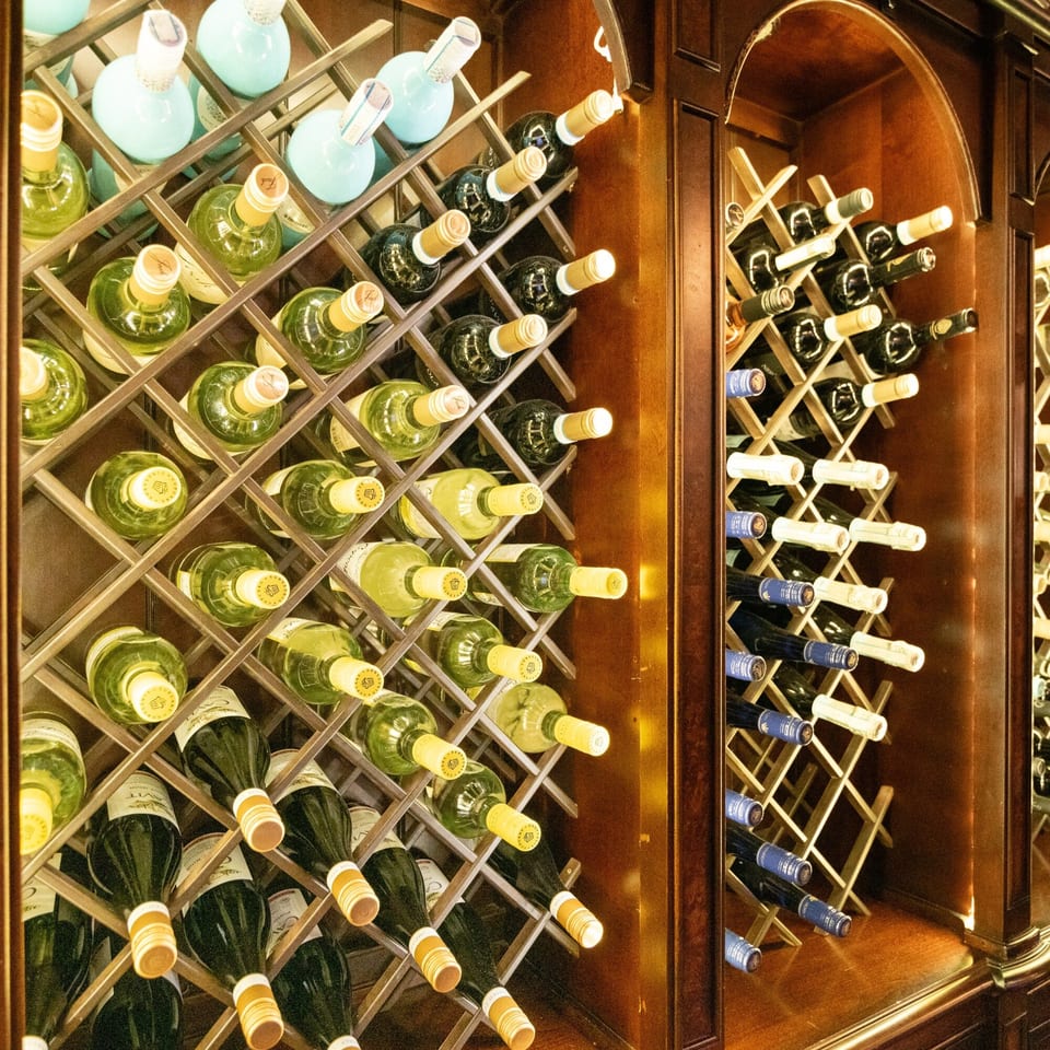 Wine bottles, both white and red, stored in wooden racks within a dark wooden cabinet.