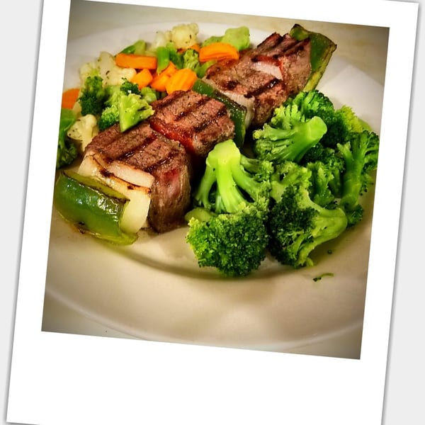 Grilled steak medallions with green peppers, onions, broccoli, cauliflower, and carrots on a white plate.